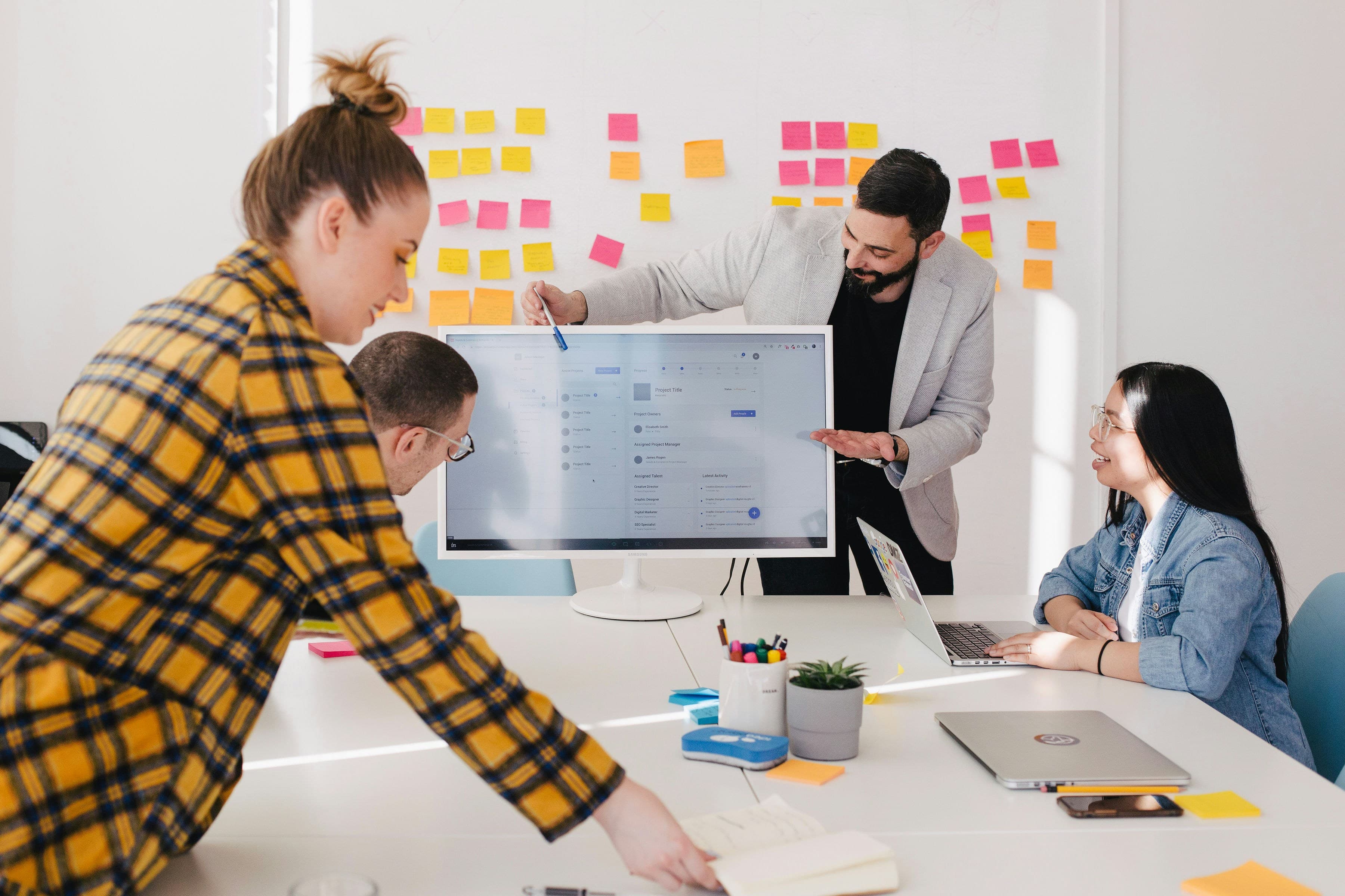 Team collaborating around a laptop in front of a wall of sticky notes